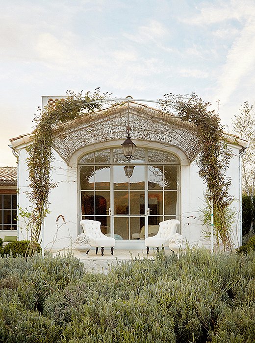 One wall of the master suite leads to a stone porch. “We like to create outdoor extensions to as many rooms as possible,” says Brooke. An arched steel trellis with some reed fencing drapes a pair of upholstered chairs from Giannetti Home.
