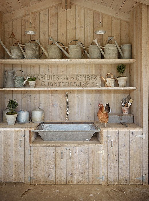 A small kitchen in the coop has a galvanized sink made from a vintage trough. “I store all of my kitchen and chicken supplies here,” says Brooke. The vintage metal watering cans come from their frequent trips to flea markets and antiques shops.
