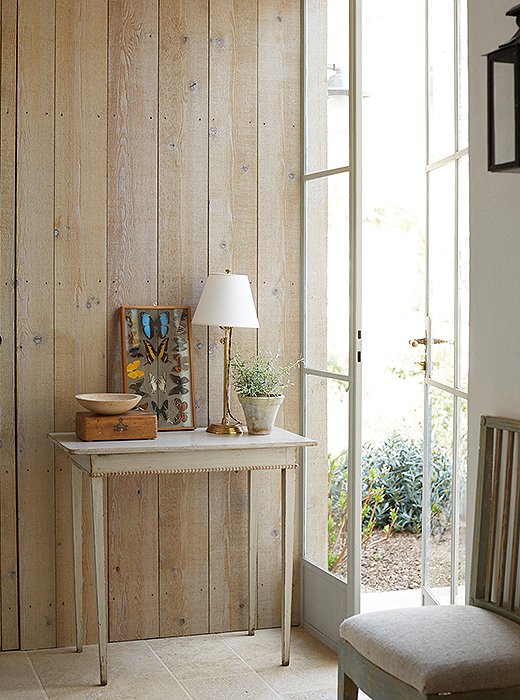 A wall of weather-grayed cedar in Brooke’s office is a backdrop for an antique Swedish table and a framed set of pressed butterflies. The limestone floor from the covered porch just outside runs through the entire room.
