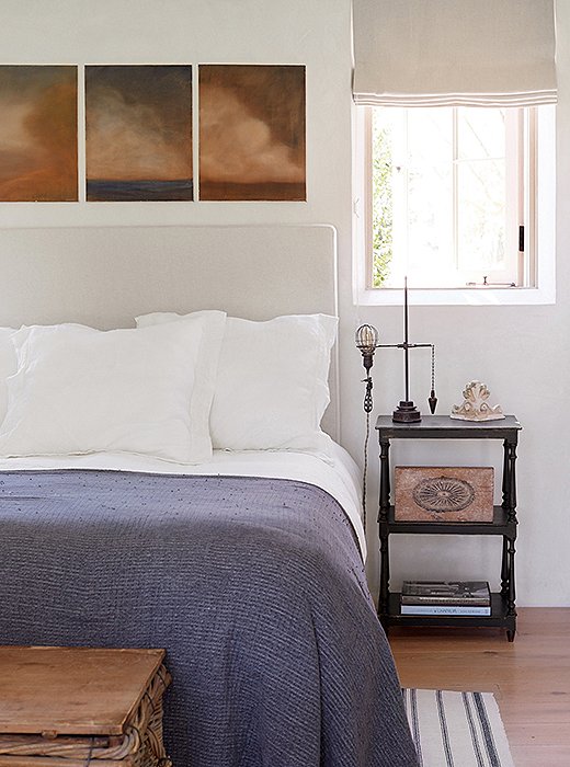 “Steve’s paintings were the inspiration for the palette of the guest bedroom,” says Brooke. A linen headboard, a woven blanket, and a striped rug add texture. The vintage industrial light with its original cloth-covered wiring is a unique bedside lamp.
 
