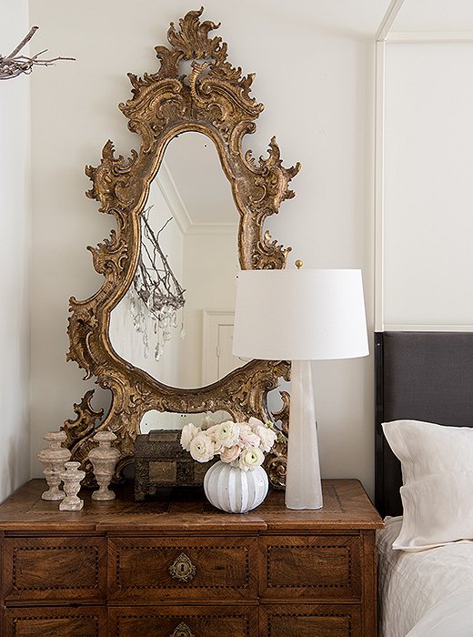 Modern-leaning, streamlined table lamps flanking the four-poster bed perfectly balance an ornate antique mirror. While the lamps match, Tara used mismatched bedside tables and wall decor on either side.
